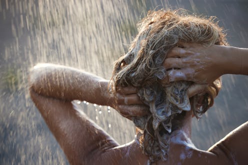 Rear view of a woman washing her hair with shampoo at shower.