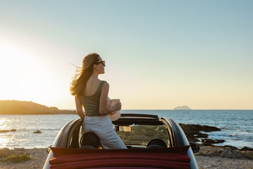 Cheerful young woman in an open-top car. She is enjoying the sunset and looking at the sea