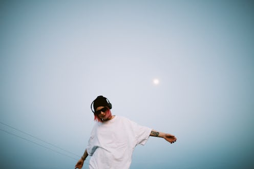 A person in a white shirt and black cap, arms outstretched, joyfully posing under a clear blue sky w...