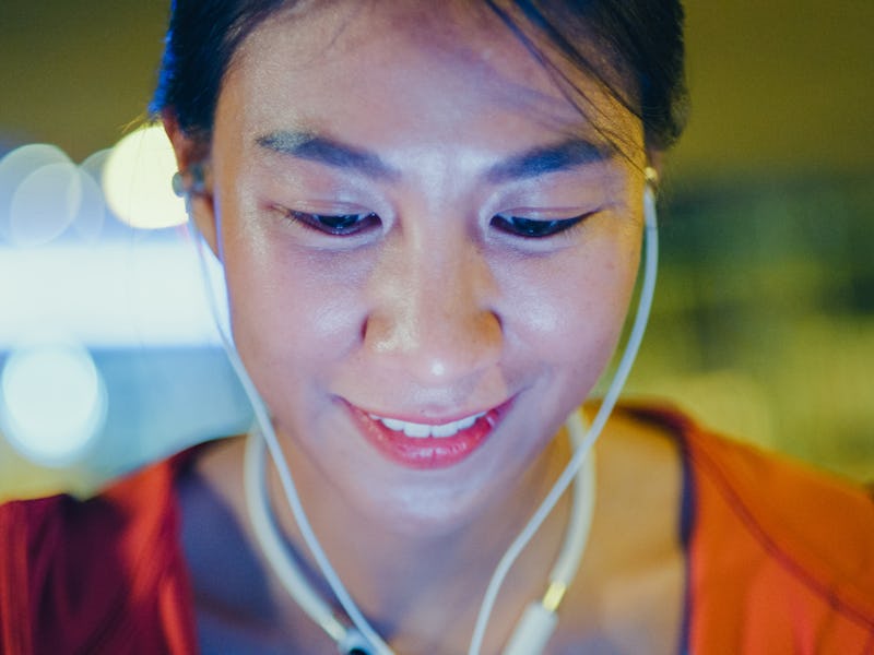 Closeup of young Asian female athlete runner listening to music with earphones on smart phone app fo...