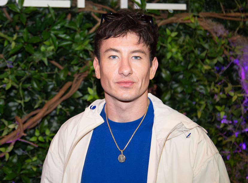 Man with brown hair wearing a blue shirt, beige jacket, and sunglasses on his head, posing in front ...