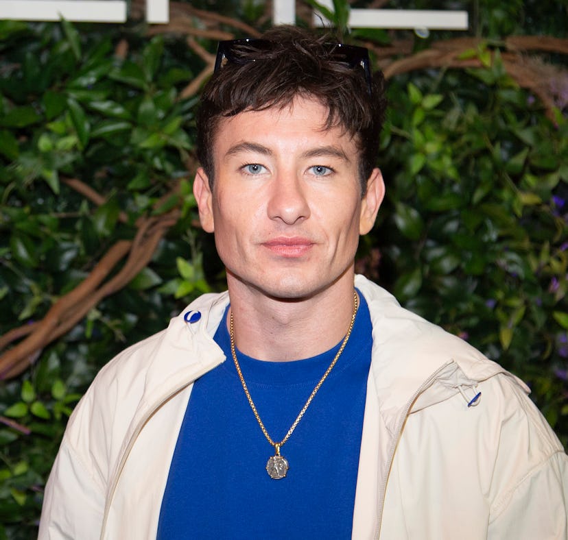 Man with brown hair wearing a blue shirt, beige jacket, and sunglasses on his head, posing in front ...
