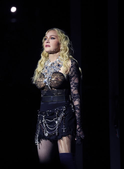 Woman in ornate costume with fishnet stockings and chain accessories, standing on stage under a spot...