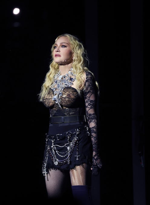 Woman in ornate costume with fishnet stockings and chain accessories, standing on stage under a spot...