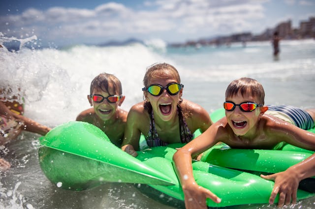 Kids are splashing and having fun on inflatable raft. Kids are shouting as a breaking wave is splash...