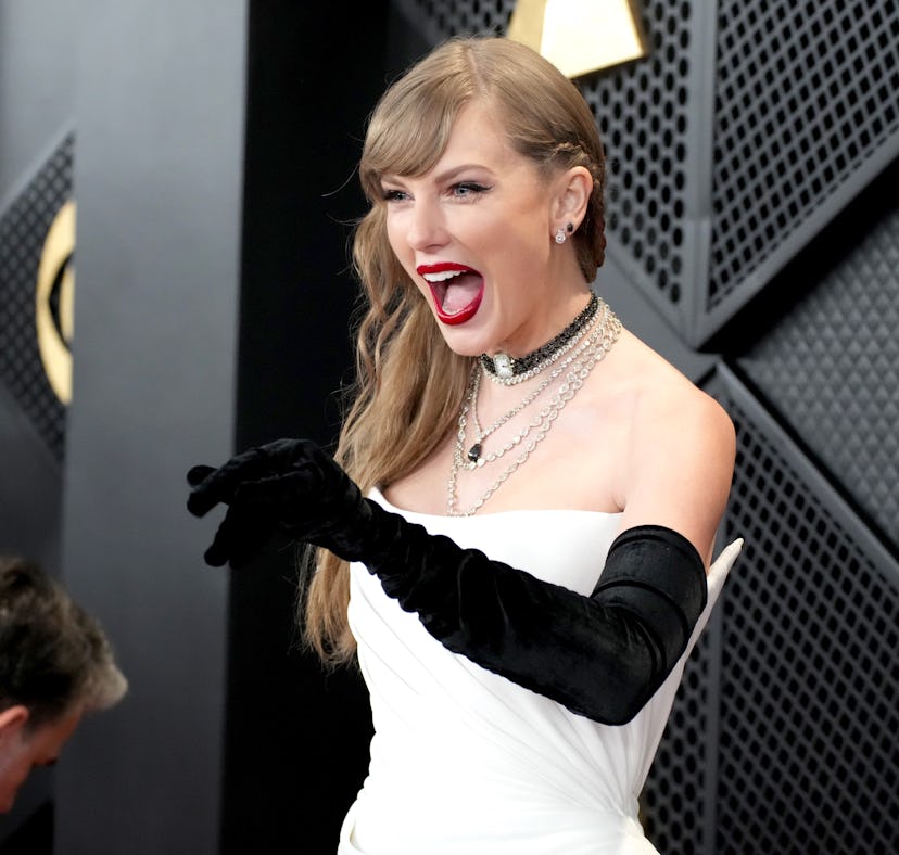 A woman in a white gown and black gloves laughing excitedly at an event. A man is seen bending down ...