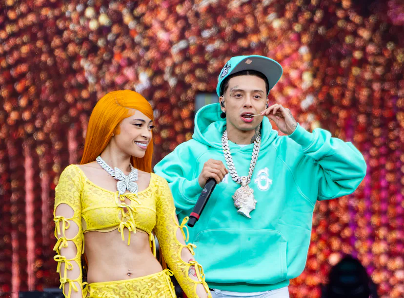 A man in a turquoise tracksuit and woman in yellow outfit performing on stage with a colorful backdr...
