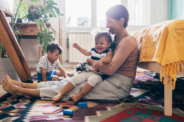 Mother holding her daughter while sitting on the floor, her son playing with wooden blocks.