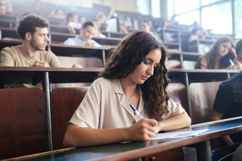 Female college student writing an exam during a class in amphitheater.