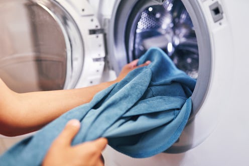 A close-up view of hands pulling blue clothes from a washing machine. The scene focuses on the actio...