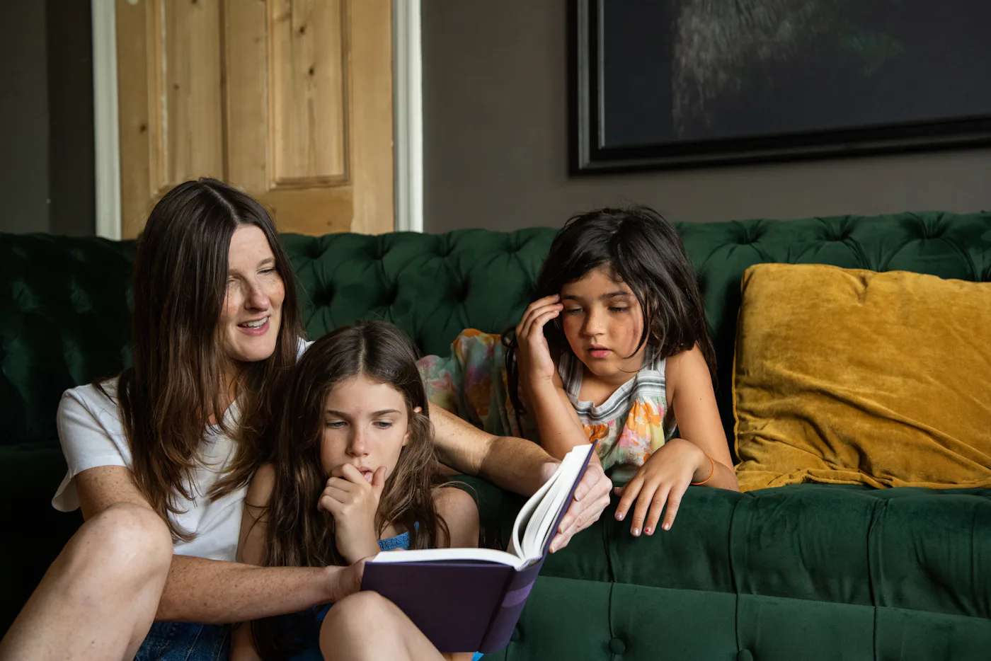 Mother reading a book to her daughters, sat on the floor