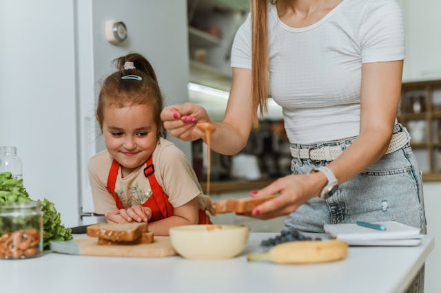 Female Child Looking Greedily At Mother Making Her Bread With Peanut Butter And Banana Slices
