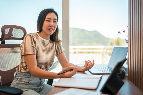Waist up image of a busy Asian female entrepreneur in comfortable clothes making a business call ...