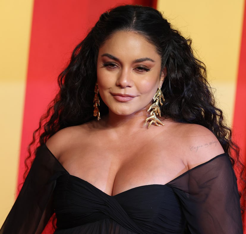 A woman in a black off-the-shoulder dress and gold earrings poses confidently against a red and yell...