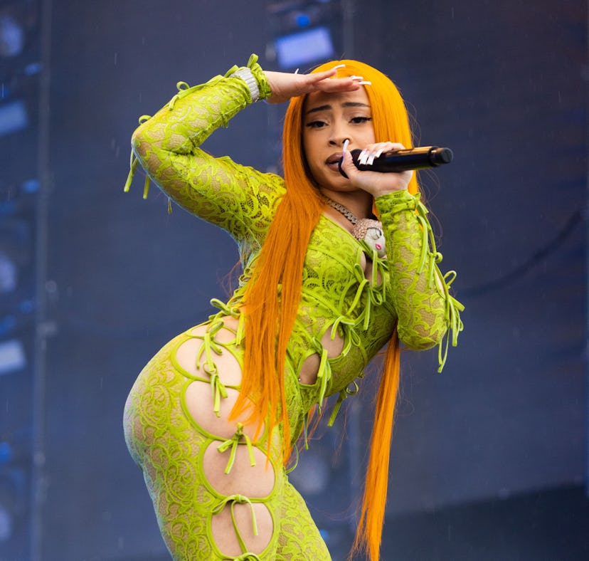 Female performer in lime green outfit and orange hair singing into a mic on stage.