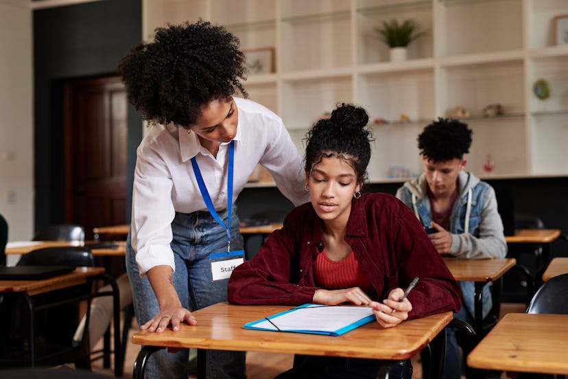 Teacher helping teenage student with paper during exam in classroom at high school