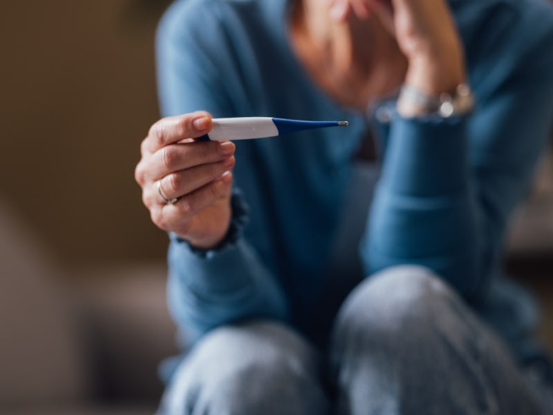 Close-up of a stressed young woman holding a negative pregnancy test, seated with head in hands, fee...