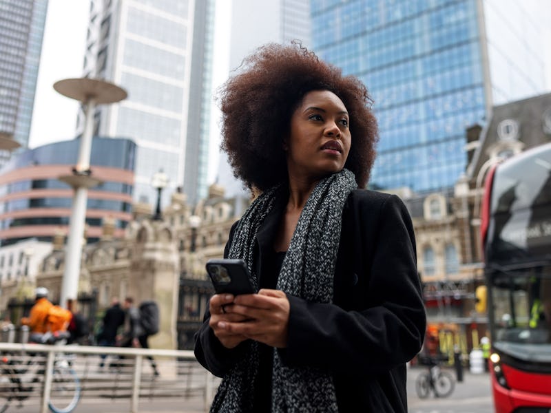 A confused adult black female checking directions on her phone and looking around. She is strolling ...