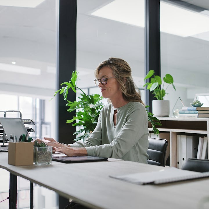 Laptop, typing and mature business woman at desk in glass office for administration or company manag...
