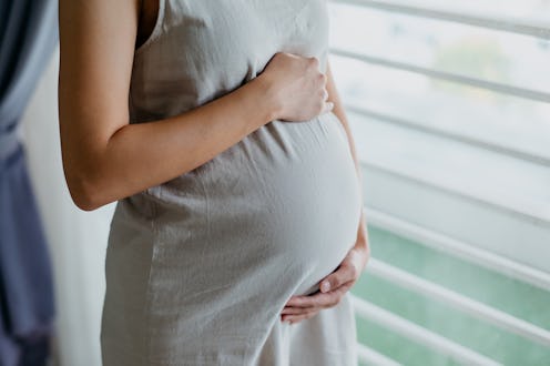 Image of an Asian pregnant woman standing and touching her belly at home