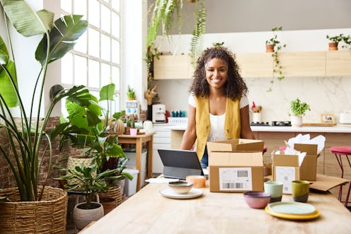 Portrait of smiling businesswoman with boxes at table. Confident female entrepreneur is at home offi...