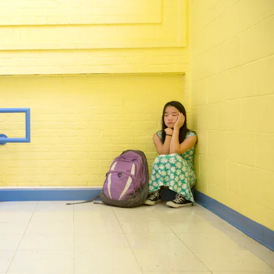 Eleven-year-old girl looks distressed while sitting all be herself in a school stairwell. A mom went to Reddit for advice on how to help her "weird kid" make friends at school.