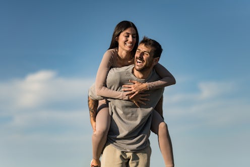 Happy young man giving his girlfriend a piggyback ride and having fun in nature on summer day with b...