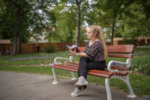 Young college girl sitting on a bench in the park and reading a book