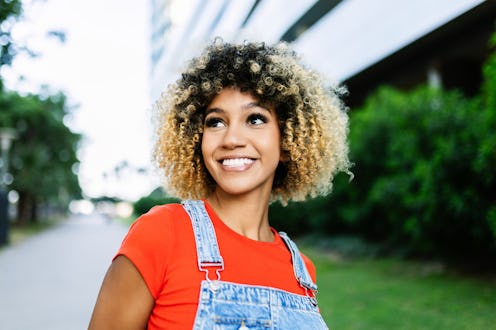 Portrait of young happy Latin American girl smiling standing over buildings outdoors.