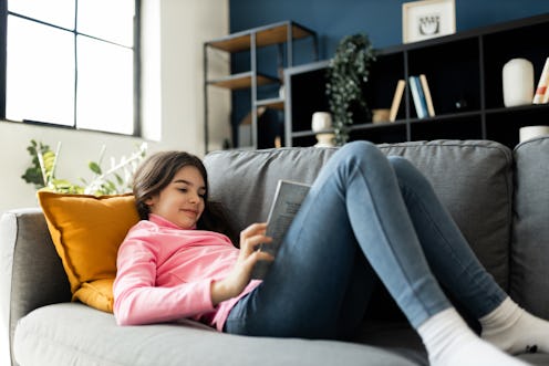 Teenage girl lying down on the sofa an enjoying reading a book.