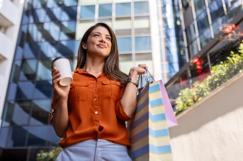 Young woman in shopping holding coffee cup and shopping bags