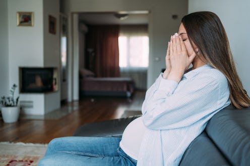 Shot of young pregnant woman suffering from headache while sitting on the sofa at home