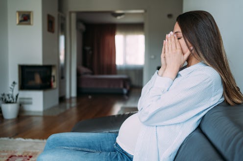 Shot of young pregnant woman suffering from headache while sitting on the sofa at home