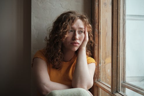 Gen z mental health. Portrait of sad upset young woman sitting by window at home, feeling lonely