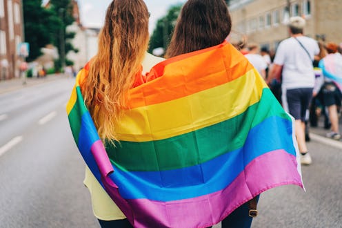 Two female friends wrapped in an LGBT+ flag at the pride parade