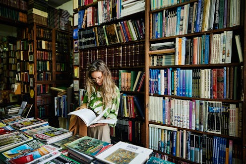 Medium wide shot of woman reading book while browsing in antique bookstore while exploring during ci...
