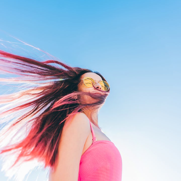 Portrait of a young woman with long pink hair flying in the wind against the sky.