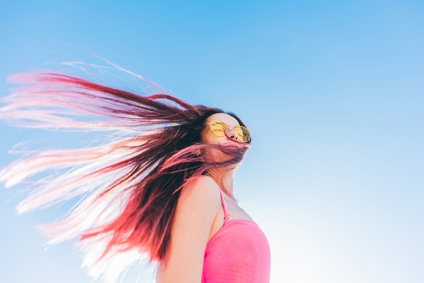 Portrait of a young woman with long pink hair flying in the wind against the sky.