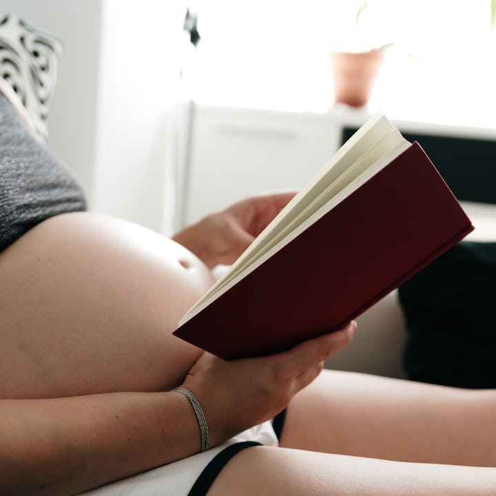Pregnant woman lying on the sofa while reading a book.