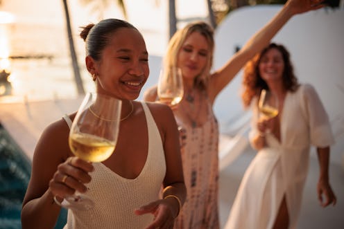 Three beautiful women enjoying having wine and dancing by the swimming pool at a luxurious villa tha...