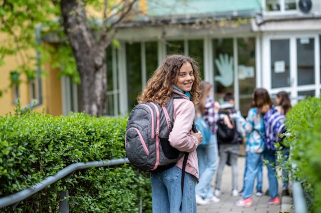 children enter the school and one girl turns and looks at the camera