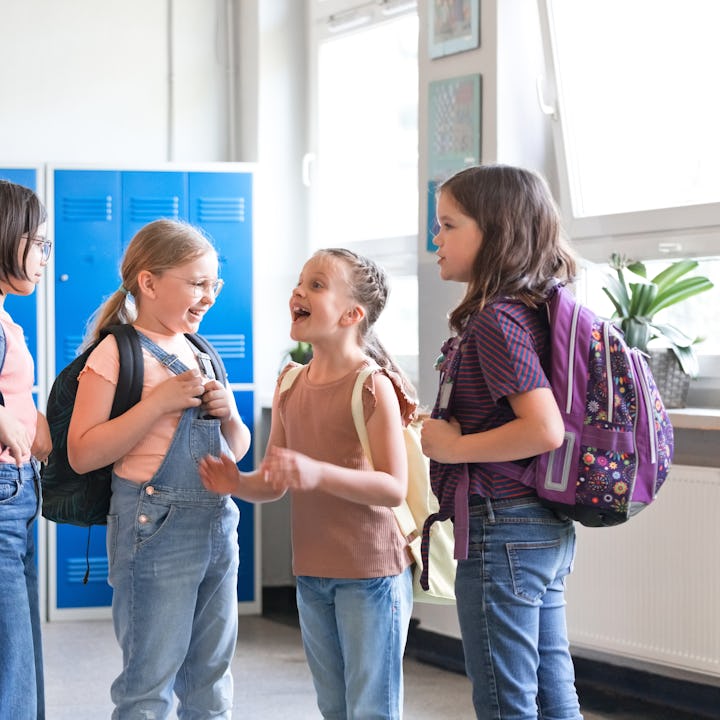 Happy girls and boy talking during break in the school corridor, standing next to lockers.