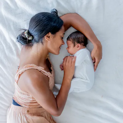 A new Mother lays on the floor beside her newborn as she gazes at him lovingly and the two rest together