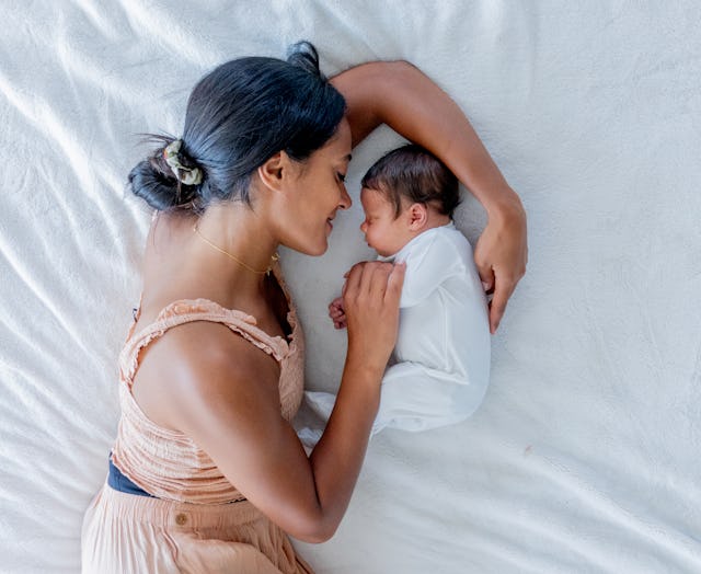 A new Mother lays on the floor beside her newborn as she gazes at him lovingly and the two rest toge...