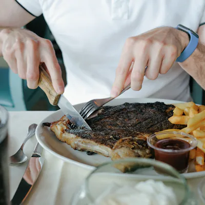 Man eating a half rack of ribs with side of fries at restaurant. A Redditor wants to know "AITAH" for eating meat while his vegetarian wife was away.