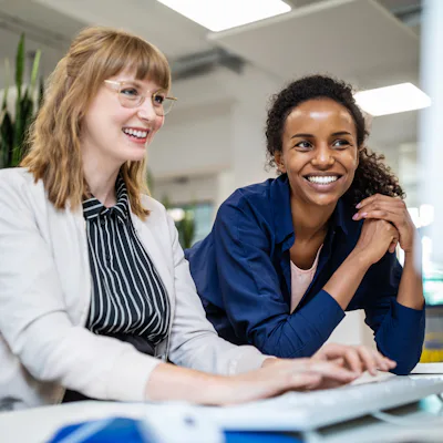 Multi-ethnic female entrepreneurs smiling while looking at computer in creative office