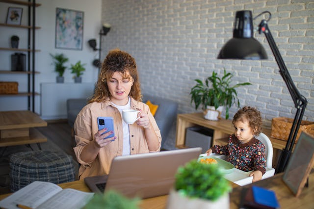 Young mother working and using phone while taking care of her baby