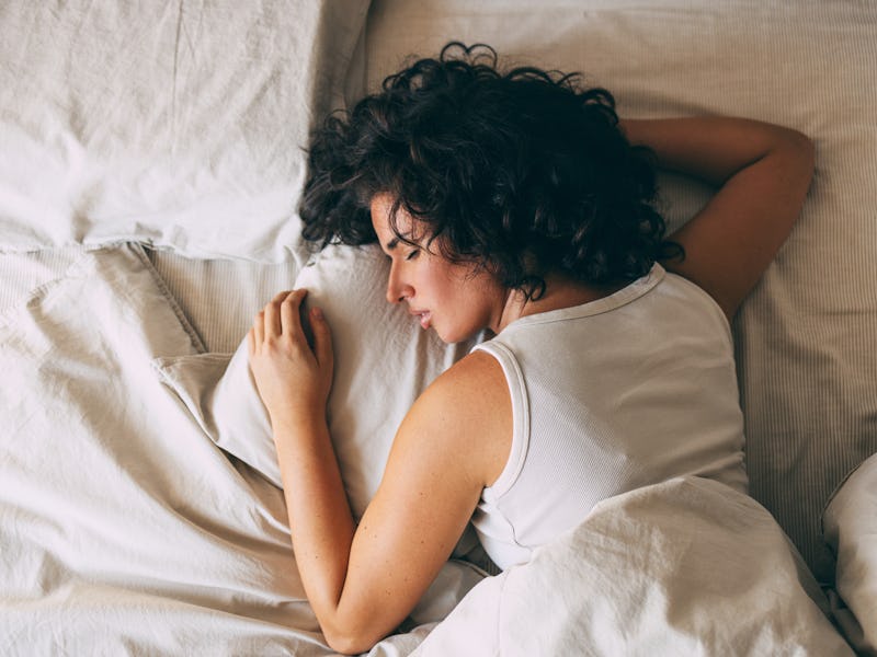 A woman with curly hair peacefully sleeping in a cozy bed, showcasing relaxation and restfulness. Pe...