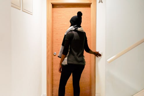rear view of a beautiful brunette woman standing at the door of a closed apartment
