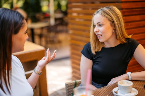 Two young women drinking coffee in a café outdoors.